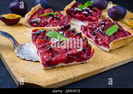 Der traditionelle deutsche Zwetschgenkuchen mit geschnittenen Pflaumen diente als Nahaufnahme auf einem rustikalen Holzbrett Stockfoto