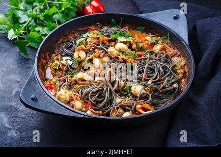 Traditionelle italienische Spaghetti al nero di seppia mit Tintenfisch-Tinte in Tomatensauce, die als Nahaufnahme in einer gusseisernen Pfanne auf einer R serviert werden Stockfoto