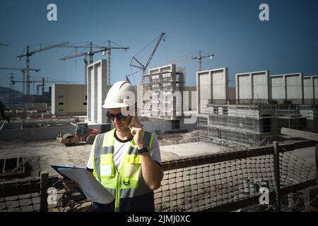 Bauingenieur ruft auf der Baustelle mit seinem Mobiltelefon an Stockfoto