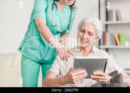Krankenschwester, die ein digitales Tablet mit einer älteren Patientin zeigt Stockfoto