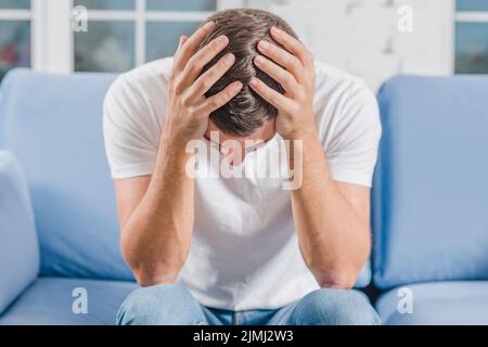 Frustrierter Mann, der unter Kopfschmerzen leidet, sitzend auf dem Sofa Stockfoto