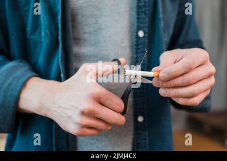 Nahaufnahme Mann s Hand schneiden Zigarette mit Schere Stockfoto