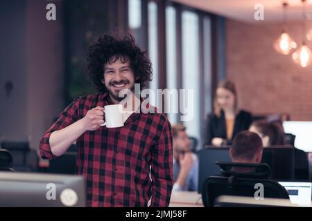 Lächelnder Geschäftsmann im Afro-Hemd, der im modernen Büro mit einer Tasse Kaffee in der Hand steht. Selektiver Fokus Stockfoto