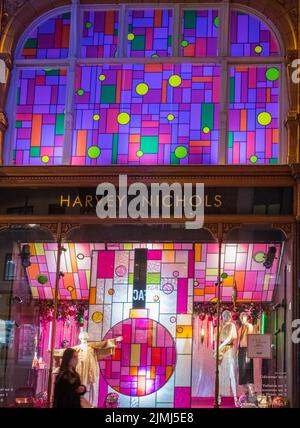 Eine Frau mit Gesichtsmaske geht am wunderschön beleuchteten Kaufhaus Harvey Nichols im Stadtzentrum von Leeds, Leeds, Großbritannien, vorbei Stockfoto