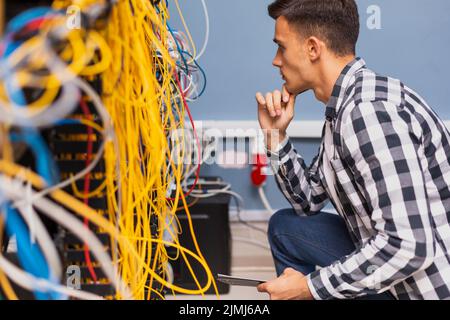 Junger Netzwerkingenieur mit Blick auf Drähte Stockfoto