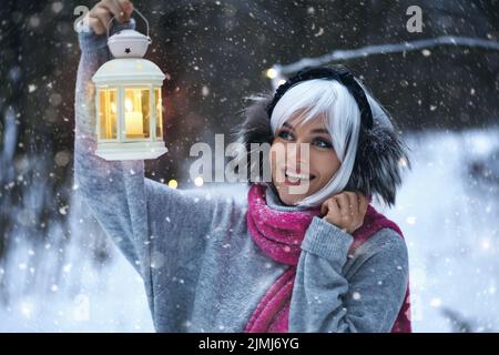 Junge Frau mit Kerzenlicht-Laterne in der Hand beim Spaziergang im verschneiten Winterwald Stockfoto