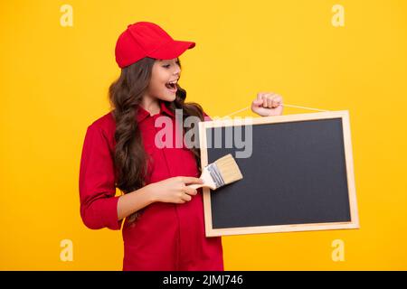 Glücklich lächelnd Teenager Mädchen Baumeister in den Aufbau von Uniform und Kappe. Malen Sie mit dem Pinsel oder der Malwalze. Arbeiter halten die Tafel isoliert an Stockfoto