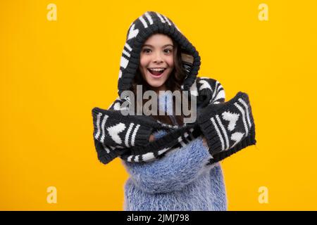 Warmer Hut mit Kapuze und Schal. Ein erstaunlicher Teenager. Schöne Teenager-Mädchen in einem Winterhut und einem warmen Pullover. Ein Kind auf einem gelben isolierten Hintergrund Stockfoto