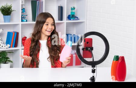 Teen girl blogger Influencer verwenden Selfie-LED-Lampe und Smartphone auf Stativ für die Herstellung von Online-Video-Tutorial, halten Haarspülung oder Shampoo-Flasche Stockfoto