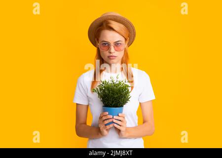 Fröhliche junge Frau mit Topfpflanze. Isolierter gelber Hintergrund, Nahaufnahme im Hochformat. Pflanzenpflege und Hausgartenarbeit. Frau pflanzt Blumen in den Topf. Stockfoto