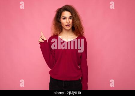 Foto von jungen schockiert schöne Brünette wellig Frau mit aufrichtigen Emotionen tragen beiläufige rosa Pullover isoliert über rosa Backgr Stockfoto