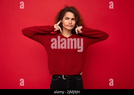 Foto von jungen unzufrieden müde attraktive Brünette wellenhaarige Frau mit aufrichtigen Emotionen tragen lässigen roten Pullover isolieren Stockfoto