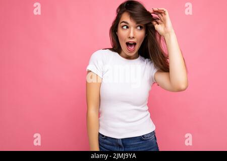 Foto-Porträt von jungen schönen positiv überrascht überrascht, schockiert Brünette Frau in weißem T-Shirt mit Mockup. Weibliche Person Stockfoto