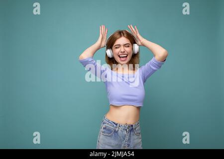 Charmante glücklich lächelnde junge blonde Frau trägt blauen Crop Top isoliert auf blauem Hintergrund mit Platz für Text tragen Whi Stockfoto