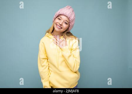 Attraktive lächelnde glückliche junge blonde Frau, die isoliert über der farbenfrohen Hintergrundwand steht, trägt jeden Tag ein stilvolles Outfit Stockfoto