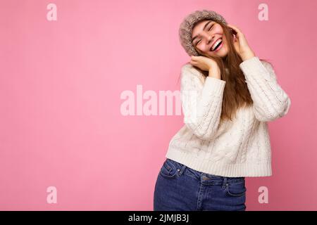 Foto von ziemlich positiv amüsant junge Brünette Frau isoliert über rosa Hintergrund Wand tragen gestrickten weißen Pullover und grau Stockfoto