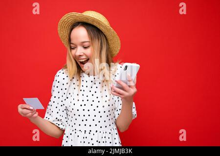 Foto von attraktiven positiv überrascht junge blonde Frau in Sommerkleidung mit Handy und halten Kreditkarte machen Payme Stockfoto