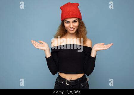 Foto von jungen positiven glücklich attraktive Brünette lockige Frau mit aufrichtigen Emotionen tragen schwarzen Crop Top und roten Hut isoliert Stockfoto