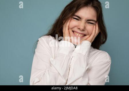 Portrait der schönen positiven fröhlich niedlich lächelnd junge Brünette Frau in casual weißes Hemd auf blauem Hintergrund mit isoliert Stockfoto