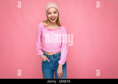 Foto von schönen glücklich lächelnd fröhlich junge blonde Frau isoliert über rosa Hintergrund Wand tragen trendige rosa Hut und rosa b Stockfoto