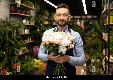 Geschäftsmann Florist mit einem Blumenstrauß in den Händen auf dem Hintergrund des Blumengeschäftes Stockfoto