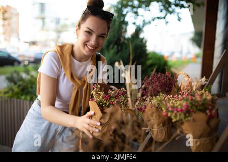 Junge schöne Brünette Frau genießt Blumen in Töpfen auf der Veranda eines Blumenladens Stockfoto