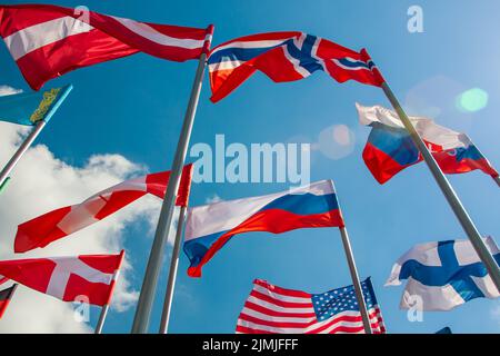 Leuchtende Flaggen verschiedener Länder gegen den blauen Himmel und Wolken Stockfoto