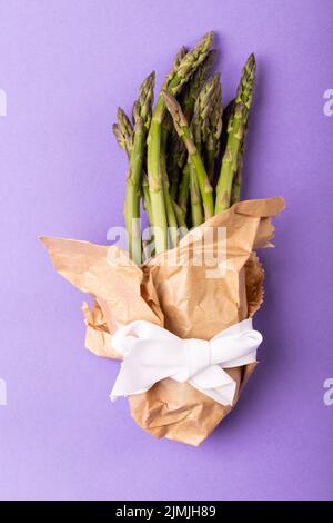 Direkt über der Ansicht von Spargelbündel in braunem Papier mit weißem Band auf violettem Hintergrund gebunden Stockfoto