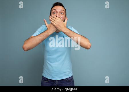 Foto eines erwachsenen gutaussehenden Brunet unrasiert Mann mit Bart mit aufrichtigen Emotionen tragen lässiges blaues T-Shirt isoliert über blauen Rücken Stockfoto