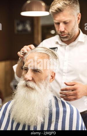 Friseur macht stilvolle Frisur für einen schönen alten Mann Stockfoto