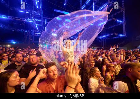 Kastellaun, Deutschland. 07. August 2022. Eine Frau im Schmetterlingskostüm tanzt beim Techno-Festival 'Nature One', während über ihnen ein Feuerwerk abgeschossen wird. Das Festival auf dem ehemaligen amerikanischen Kreuzraketen-Stützpunkt in Hunsrück konnte wegen der Pandemie zwei Jahre lang nicht stattfinden. In diesem Jahr erwarten die Veranstalter rund 60000 Besucher. Quelle: Thomas Frey/dpa/Alamy Live News Stockfoto