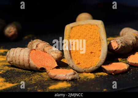 Kurkuma Pulver in einem Holzlöffel und Wurzeln auf einem dunklen Tisch (Curcuma longa), Kurkuma Stockfoto