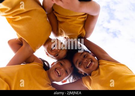 Direkt unten Porträt von fröhlichen multirassischen Grundschüler, die sich gegen den Himmel drängen Stockfoto