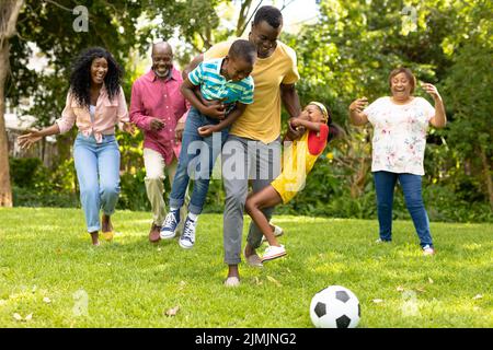 Spielerische afroamerikanische Familie mit mehreren Generationen, die am Wochenende gemeinsam im Hinterhof Fußball spielt Stockfoto