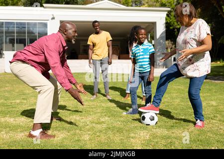 Glückliche afroamerikanische Familie mit mehreren Generationen, die am sonnigen Tag gemeinsam vor dem Hof Fußball spielt Stockfoto