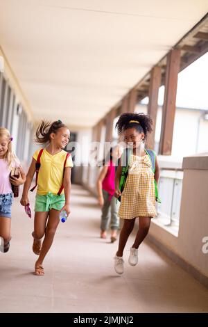In voller Länge fröhliche multirassische Grundschüler gehen im Flur Stockfoto