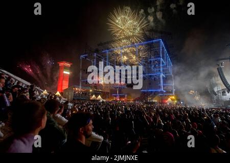 Kastellaun, Deutschland. 07. August 2022. Raver tanzen beim Techno-Festival „Nature One“, während über ihnen ein Feuerwerk abgeschossen wird. Das Festival auf dem ehemaligen amerikanischen Kreuzraketen-Stützpunkt in Hunsrück konnte wegen der Pandemie zwei Jahre lang nicht stattfinden. In diesem Jahr erwarten die Veranstalter rund 60000 Besucher. Quelle: Thomas Frey/dpa/Alamy Live News Stockfoto