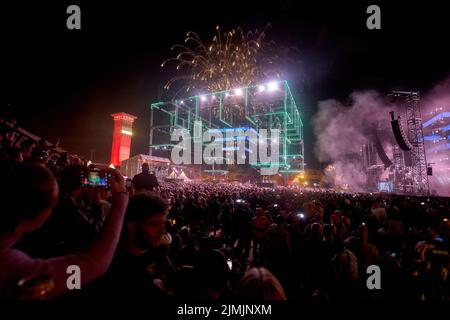 Kastellaun, Deutschland. 07. August 2022. Raver tanzen beim Techno-Festival „Nature One“, während über ihnen ein Feuerwerk abgeschossen wird. Das Festival auf dem ehemaligen amerikanischen Kreuzraketen-Stützpunkt in Hunsrück konnte wegen der Pandemie zwei Jahre lang nicht stattfinden. In diesem Jahr erwarten die Veranstalter rund 60000 Besucher. Quelle: Thomas Frey/dpa/Alamy Live News Stockfoto