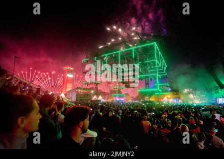 Kastellaun, Deutschland. 07. August 2022. Raver tanzen beim Techno-Festival „Nature One“, während über ihnen ein Feuerwerk abgeschossen wird. Das Festival auf dem ehemaligen amerikanischen Kreuzraketen-Stützpunkt in Hunsrück konnte wegen der Pandemie zwei Jahre lang nicht stattfinden. In diesem Jahr erwarten die Veranstalter rund 60000 Besucher. Quelle: Thomas Frey/dpa/Alamy Live News Stockfoto