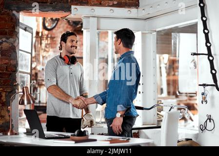 Treffen Sie sich und machen Sie Ihr Unternehmen zum Erfolg. Zwei junge Geschäftsleute schütteln sich in einem Büro in ihrer Werkstatt die Hände. Stockfoto