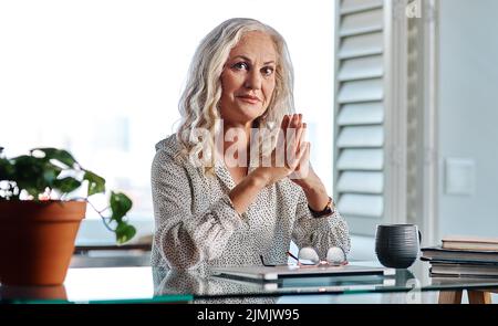 Als Geschäftsfrau muss ich weiter arbeiten. Ein beschnittenes Porträt einer attraktiven Geschäftsfrau, die bei der Arbeit mit den Händen zusammen sitzt Stockfoto