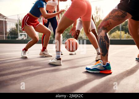 Wo die Hauptaktion ist. Eine vielfältige Gruppe von Sportlerinnen spielen ein Wettkampfspiel des Basketballs zusammen während des Tages. Stockfoto