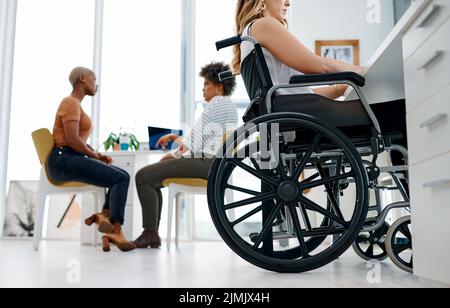 Waren alle ein großer Teil des Unternehmenserfolges. Eine Frau im Rollstuhl, die in einem Coworking Space arbeitet. Stockfoto