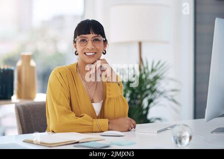 Ziele nacheinander erreichen. Das verkürzte Porträt einer attraktiven jungen Geschäftsfrau, die allein in ihrem Büro mit der Hand auf dem Kinn sitzt. Stockfoto