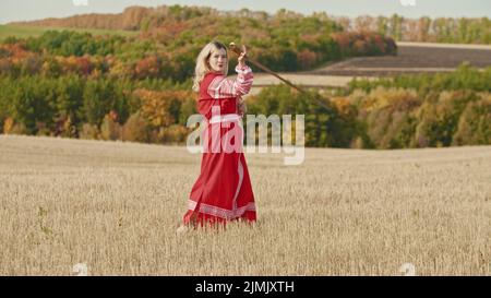Training im Herbstfeld - eine kriegerische Frau schwingt mit einem Schwert - und schaut in die Kamera Stockfoto