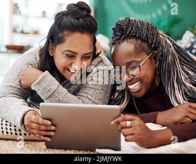 Verbringen Sie Ihre Zeit mit Menschen, die Sie zum Lachen bringen. Zwei junge Frauen benutzen ein digitales Tablet zusammen auf dem Boden zu Hause. Stockfoto