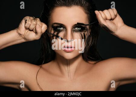 Frau mit Make-up-Flecken auf ihrem Gesicht und zerbrochenen Mascara-Bürsten Stockfoto