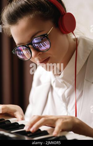 Junge Komponistin mit einer Spiegelung der Klaviertasten in einer Brille Stockfoto