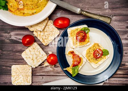 Quadratische Reiscracker mit Hummus und Kirschtomaten auf einem Teller. Tomaten, Cracker auf einem rustikalen Tisch und eine Platte mit Hummus. Natürlich und gesund f Stockfoto