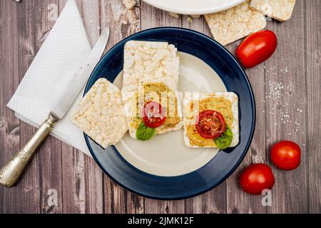 Quadratische Reiscracker mit Hummus und Kirschtomaten auf einem Teller. Tomaten, Cracker auf einem rustikalen Tisch und eine Platte mit Hummus. Natürlich und gesund f Stockfoto